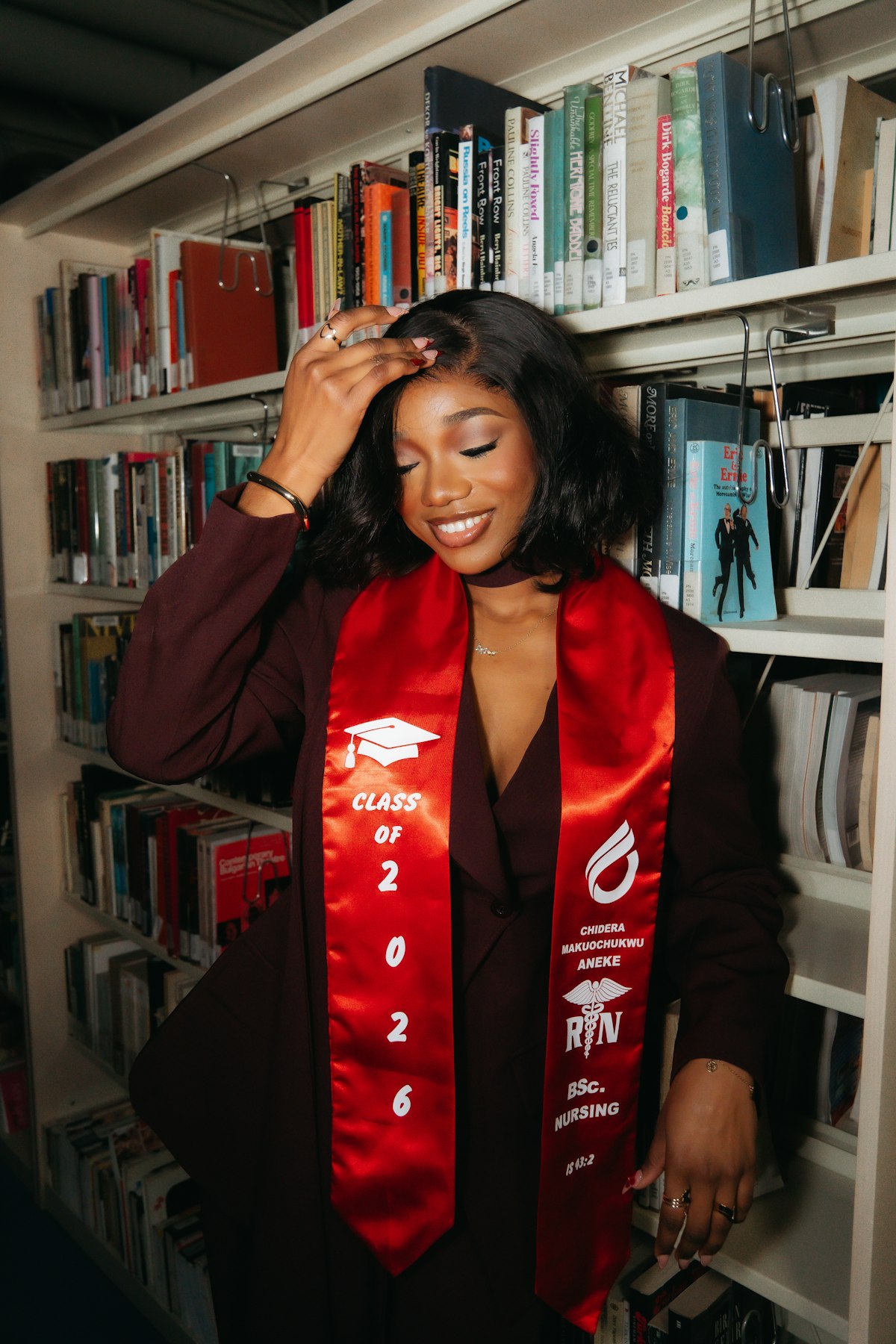 Young graduate woman in academic attire by bookshelves