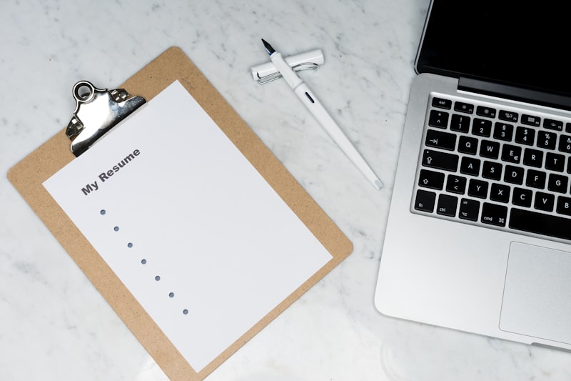 Person writing on paper documents at desk with laptop